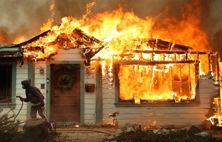 Homeowner holds a garden hose outside his home as it becomes engulfed in flame