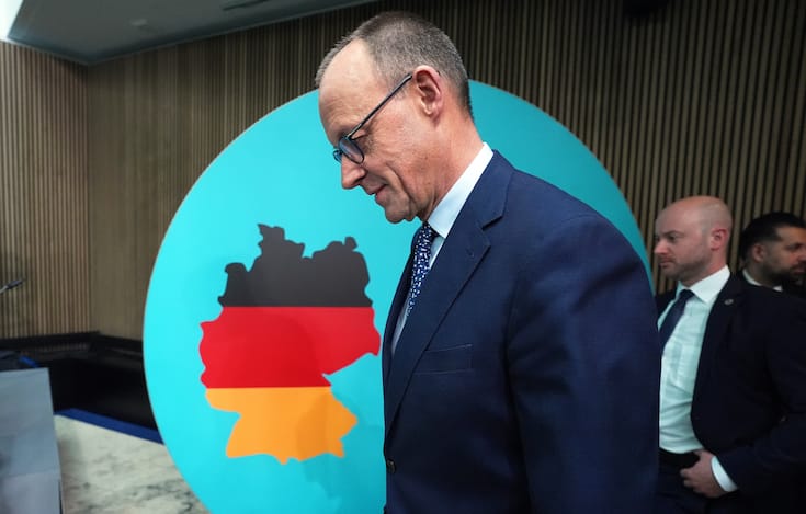 Friedrich Merz walks in front of a board showing the shape of Germany colored in with its flag colors