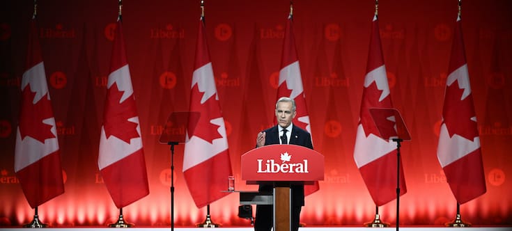 Mark Carney at the podium addressing crowd with Canadian flags in the back