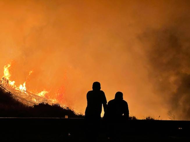 People sit watching forest burn with orange hazy background